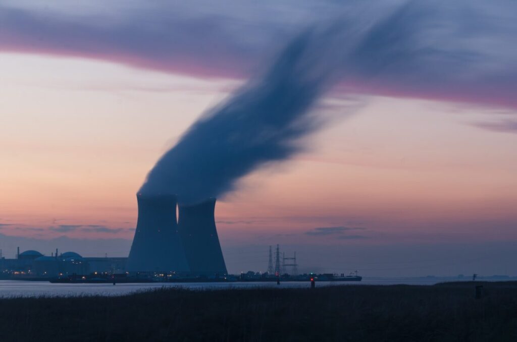 skyline photography of nuclear plant cooling tower blowing smokes under white and orange sky at daytime